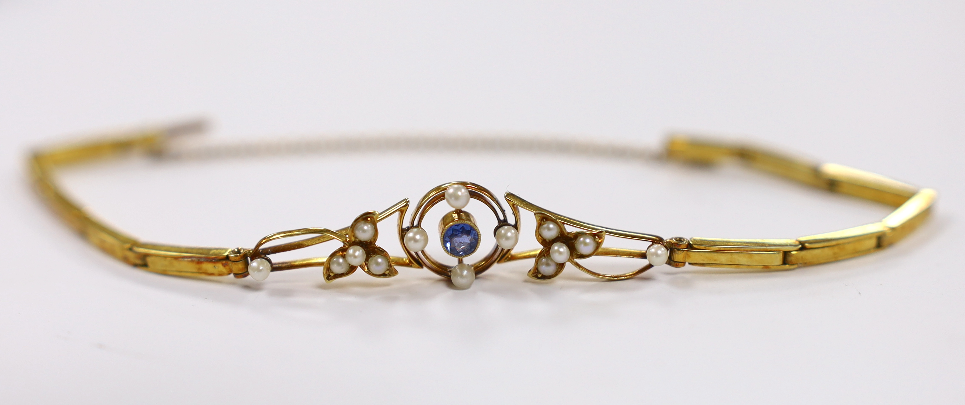 An Edwardian 15ct, sapphire and seed pearl cluster set expanding link bracelet, with safety chain, 16cm, gross weight 7.1 grams.